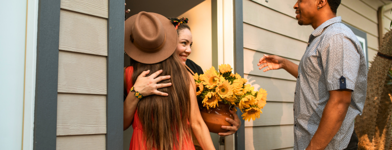 Man and woman at the front door of a house embracing a female that is standing at the door holding flowers