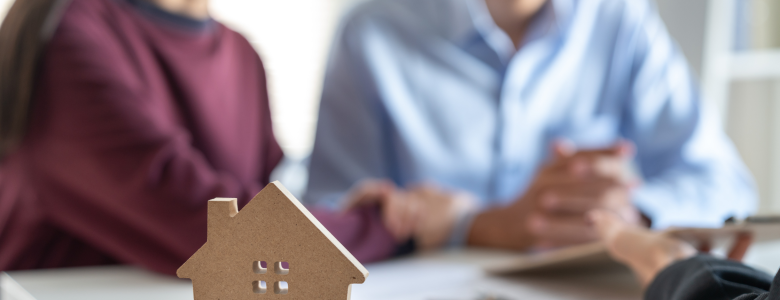 man and a woman sitting at a desk with home loan papers and a house model sitting in front of them